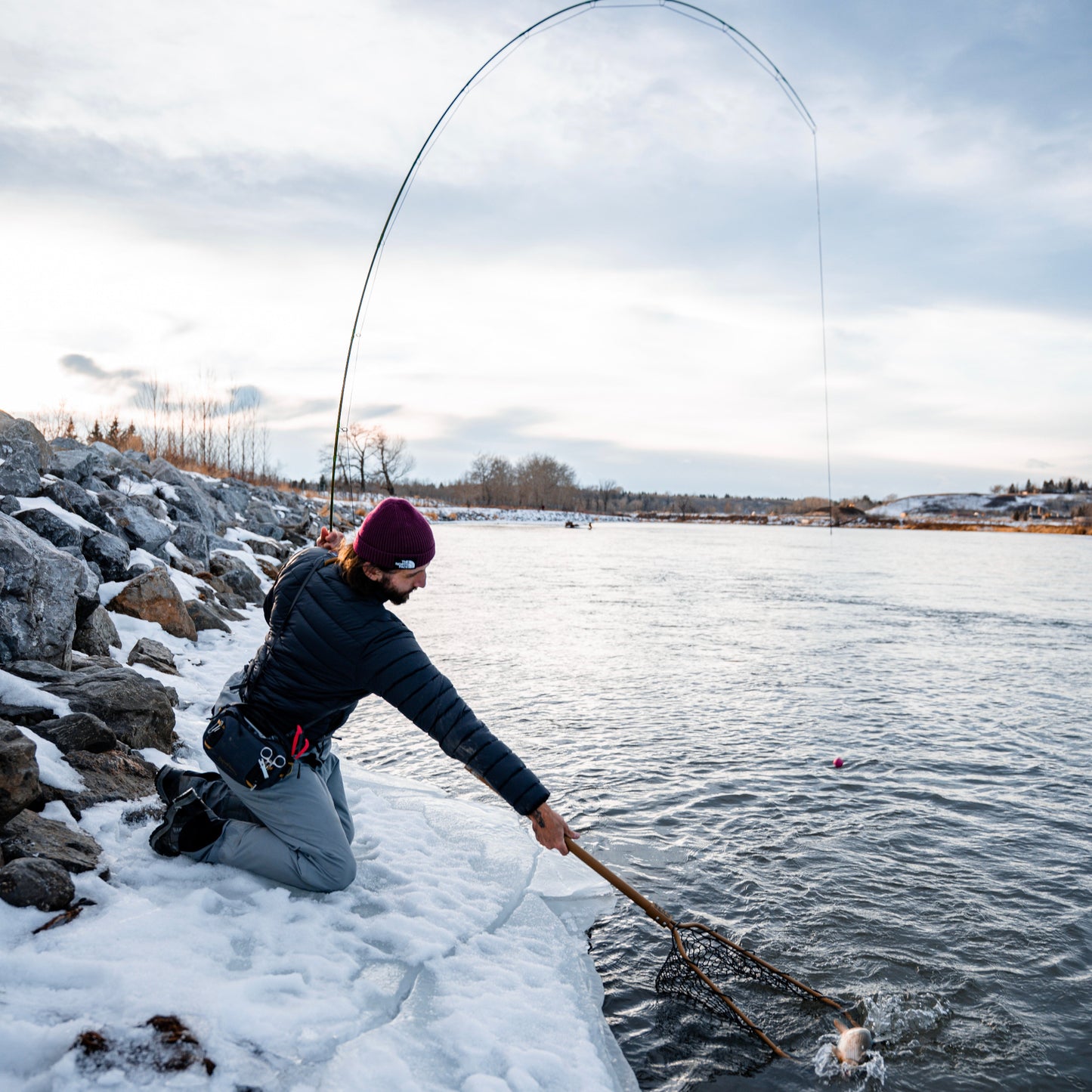 Person fly fishing on a frozen lake with a rod and net.